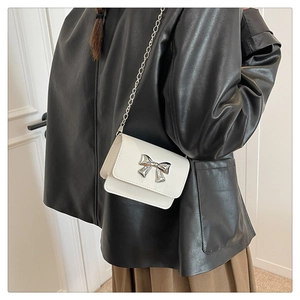 Close-up of white mini crossbody bag featuring a silver metal bow and chain strap