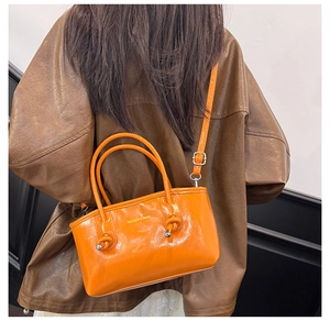 Detail of bright orange patent leather tote bag with FASHION & BAGS text and knotted handles