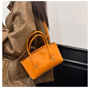 Detail view of glossy orange tote bag featuring fashion text and adjustable shoulder strap