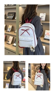 White backpack with red bow detail and leopard print bear charm in a library setting