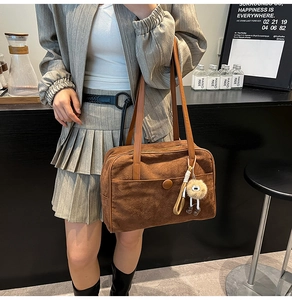 Detail of a brown suede tote bag with leather straps and a plush ball charm accessory