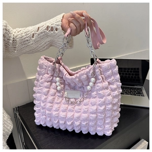 Detail van de roze geplooide handtas met parelhangers en een zilveren bloemvormige hanger