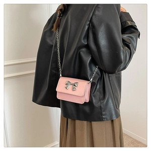 Detail of pink mini crossbody bag with silver bow and chain strap on a model