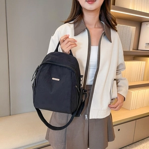 Detailansicht eines schwarzen Nylon-Minirucksacks mit Metalllogo und praktischem Tragegriff