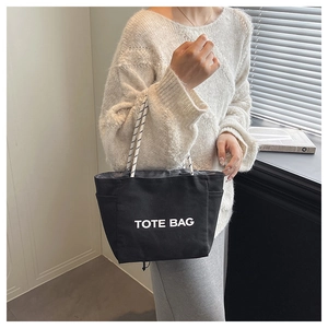 Detailed view of black canvas tote bag with woven handles and white printed text