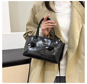 Detail of glossy black leather tote bag featuring knot accents and fashion typography