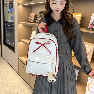 Detail view of white polka dot backpack with red bow and plush charm on zipper