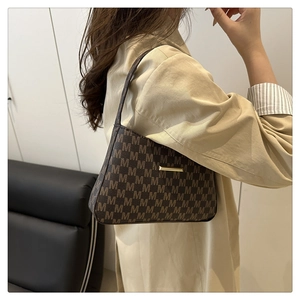 Detail of dark brown leather armpit bag with M-pattern print and gold metal bar