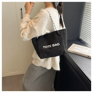 Macro detail of black canvas tote bag showing white letter print and woven handles