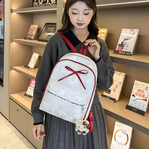 Close-up of white backpack with red bow, gold butterfly print and cute cat charm