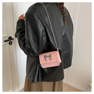 Mini pink crossbody bag with silver bow buckle and chain strap on a stylish model