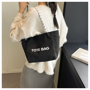 Detail of a black canvas tote bag with woven rope handles and white printed lettering