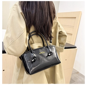 Model wearing a black glossy tote bag with gold lettering over a classic beige trench coat