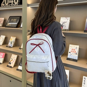 Close-up of white patent leather backpack with red bow and plush leopard charm detail