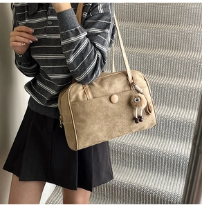 Detail of khaki suede shoulder bag featuring magnetic pocket and plush charm on a strap