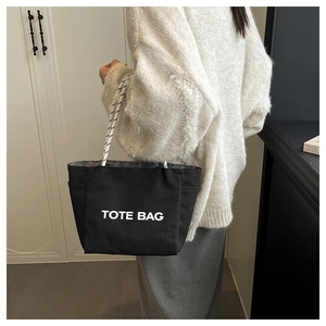 Detail of black canvas tote bag with white TOTE BAG print and rope handles on shoulder