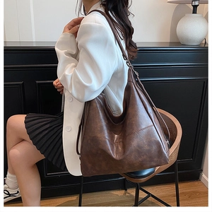 Detail of dark brown large capacity faux leather tote bag worn as a shoulder bag