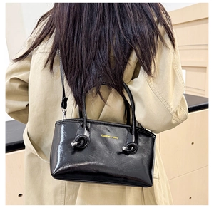 On-body view of a black glossy leather tote bag styled with a classic beige trench coat