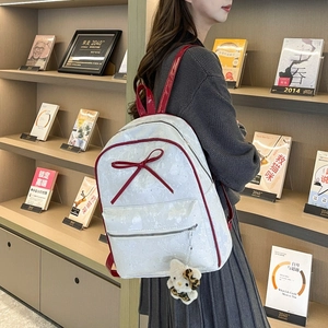 Detail of white and red butterfly backpack with a plush cat charm in a cozy bookstore