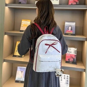 Detail of white backpack featuring red leather trim, bow accent and butterfly textures