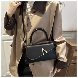 Detail der schwarzen Lederhandtasche mit goldener A-Schnalle getragen zu einem beigen Trenchcoat
