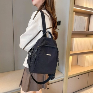 Detailansicht des schwarzen Reise-Rucksacks mit robustem Stoff und Metall-Logo-Plakette