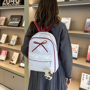 Detail of a white glitter backpack with red bow and kitty plush charm in a library setting