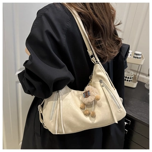 Detail of cream shoulder bag with silver zipper, long tassels and plush lamb charm