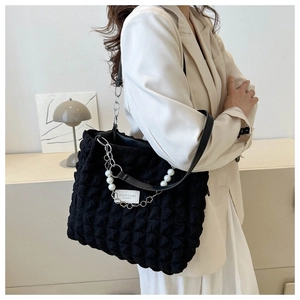Detail van zwarte bubbeltextuur tas met parelketting en vierkante logopatch
