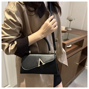 Detail of a chic black square handbag featuring a prominent gold V-shaped metal lock closure