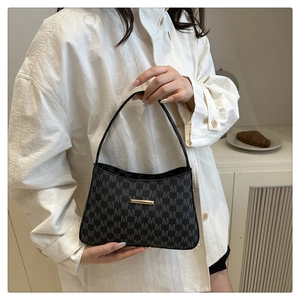 Detail of black monogram bucket bag with gold metal trim worn over a white shirt