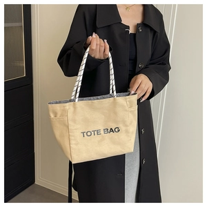 Detail of khaki canvas tote bag with black letter print and striped rope handles