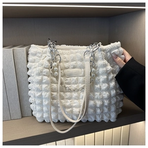 Detail van witte shopper met bubbeltextuur en elegante parel- en kettingbanden
