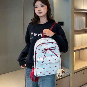 Close-up of white backpack with red bow prints and a plush cat charm detail