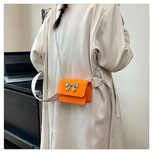 Detail of bright orange mini leather crossbody bag with silver bow on model