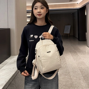 Detailansicht des cremeweißen Nylon-Rucksacks mit Metall-Logo und Reißverschlusstasche