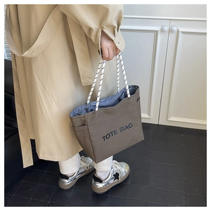 Brown canvas tote bag detail showing thick black and white rope handles and TOTE BAG print