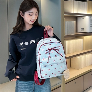 Detail of white backpack with red bow prints and a cute plush bear charm on the zipper