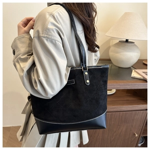 Detail of a large black quilted tote bag with suede texture and metal tag detail