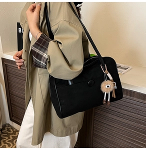 Detail view of large black canvas shoulder bag with plush pendant and long leather strap