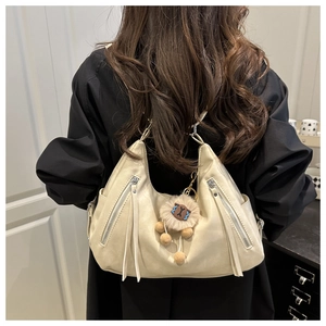 Detail of cream crescent shoulder bag with tassel zippers and plush lamb charm