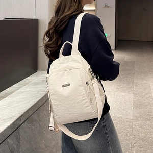 Detail eines cremefarbenen Nylon-Rucksacks mit Reißverschlüssen und Metall-Logo
