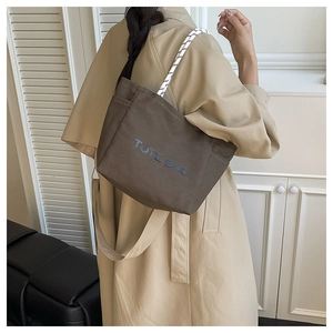 Detail of a brown canvas tote bag featuring rope handles and printed letters on the side