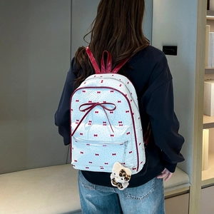 Detail of white backpack with red bow print, leather bow accent, and plush leopard charm