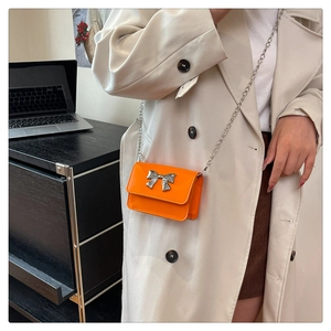Detailed view of an orange crossbody bag with a silver bow and metal chain strap