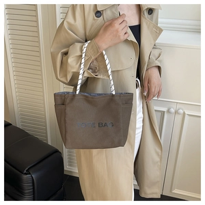Detailed view of deep brown canvas tote bag with woven handles and printed letter logo