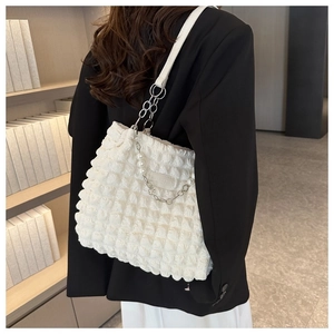 Detail van witte tas met bubbeltextuur, parels en een zilverkleurige metalen ketting