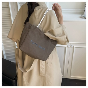 Detail of a brown canvas tote bag with letter print and woven rope handles on a model