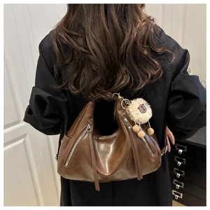 Detail of a brown crescent bag with plush lamb pendant on a model in a black jacket