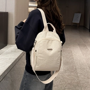 Detailansicht eines cremefarbenen Nylon-Rucksacks mit Metalllogo und breiten Gurten